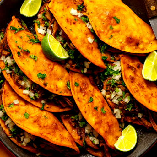 Birria tacos served with dipping consomé in a ceramic pot on a wooden counter.