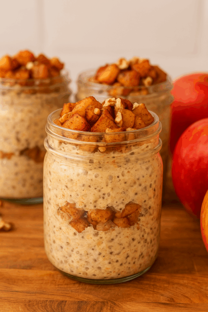Close-up shot of apple pie overnight oats in glass jars, showing layers of oats, cinnamon apples, and protein-rich yogurt with golden granola topping.