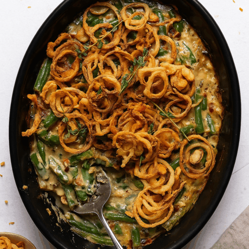 Black baking dish with green bean casserole topped with crispy onion rings, sitting on a white table background, unbaked and creamy