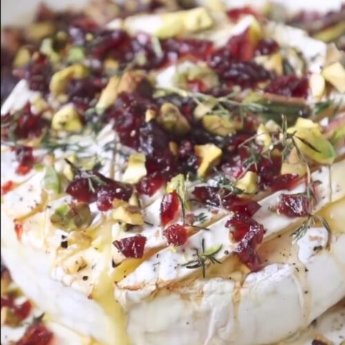 Warm baked brie topped with pistachios, cranberries, honey, and thyme on a rustic wooden board — the perfect festive Christmas appetizer.