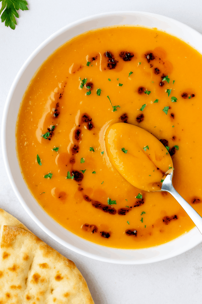 Creamy high protein Turkish lentil soup in a white bowl, made with red lentils and spices, garnished with herbs and olive oil, perfect for a cozy healthy meal.