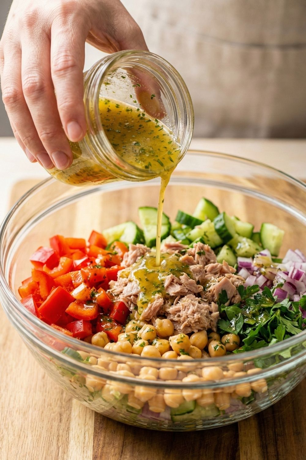 Mixing flaked tuna, chickpeas, and chopped vegetables in a large glass bowl for a no-reheat healthy salad.