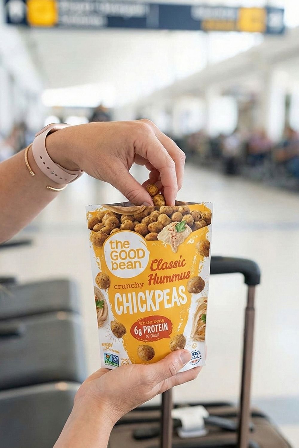 Hand holding a bag of The Good Bean Crunchy Chickpeas at the airport. A vegan, high-fiber, and crunchy alternative to chips for airplane travel.