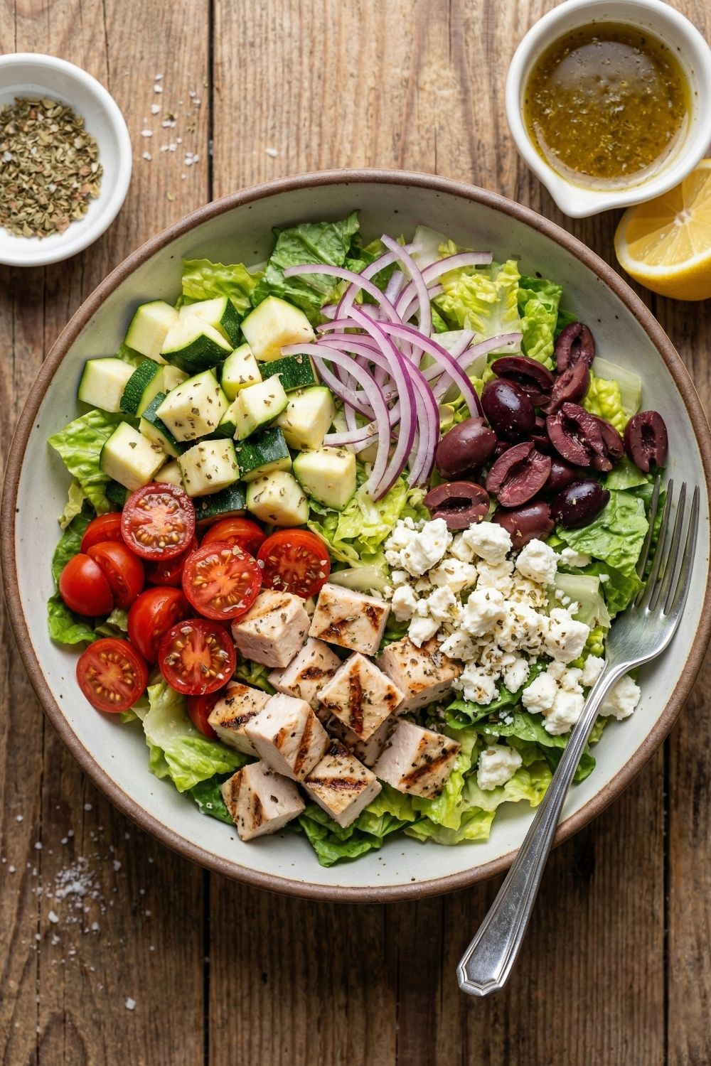 Close-up of a healthy Mediterranean chopped salad containing grilled chicken breast, feta cheese crumbles, black olives, cherry tomatoes, and romaine lettuce in a large white serving bowl.