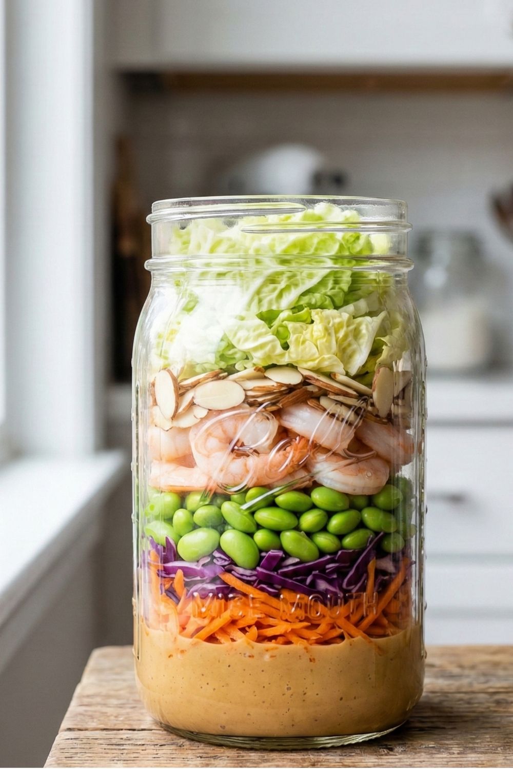 Thai-inspired mason jar salad featuring layers of shrimp, shelled edamame, shredded carrots, and purple cabbage with peanut dressing.
