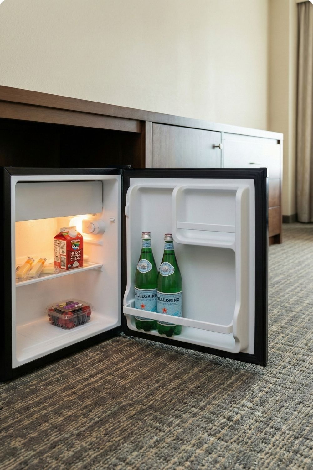 Stocked hotel mini fridge with keto essentials like sparkling water, heavy whipping cream, and cheese sticks.