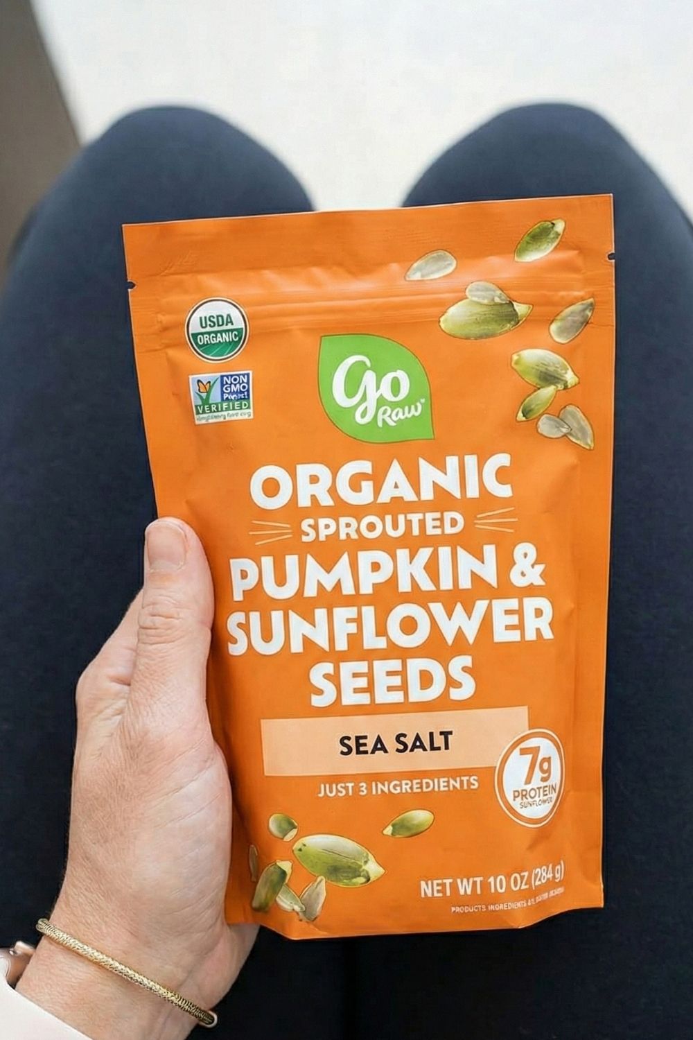 Woman holding a bag of Go Raw Sprouted Pumpkin Seeds. A magnesium-rich, nut-free high-protein snack perfect for anxious flyers.