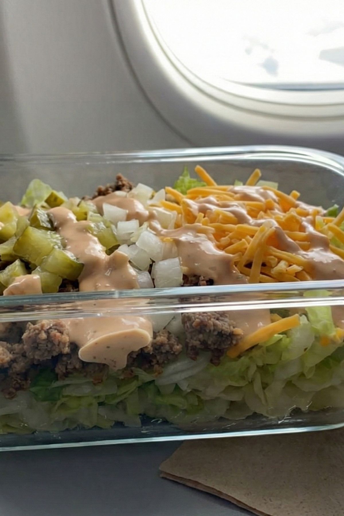 Healthy low carb Big Mac Salad meal prep in a plastic container for a high protein airplane meal.