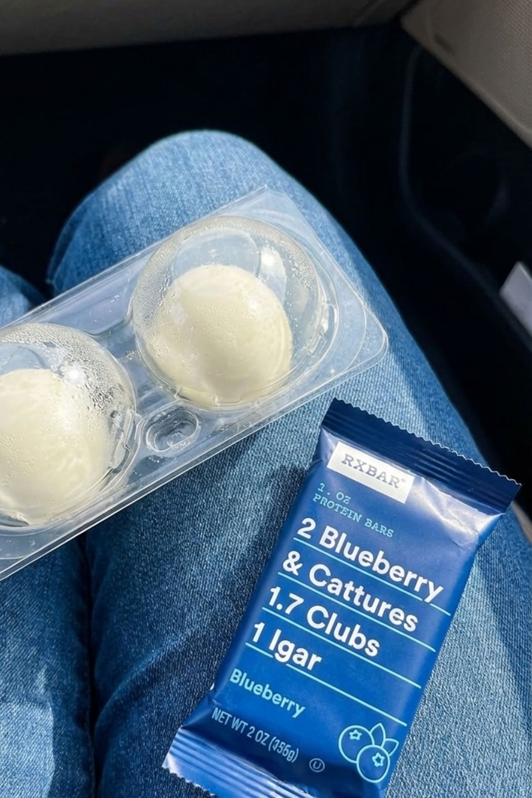 Pack of fresh hard-boiled eggs and a blueberry RXBAR protein bar sitting on a lap, showing healthy refrigerated gas station finds.