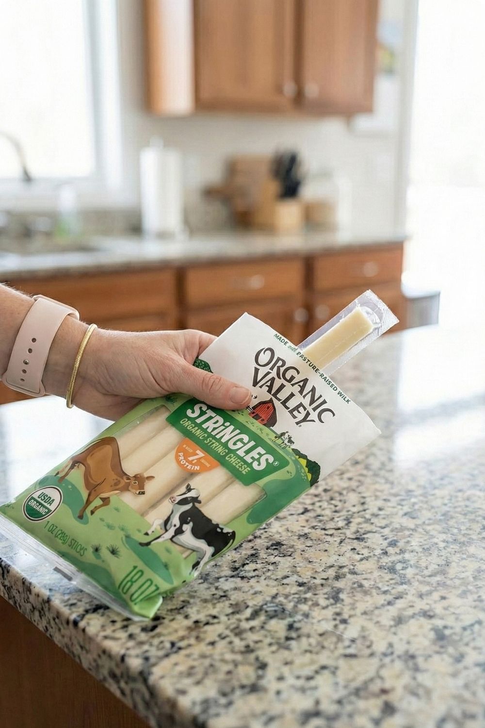 Hand holding an Organic Valley Stringles cheese stick. A keto-friendly, calcium-rich solid food snack allowed by TSA.