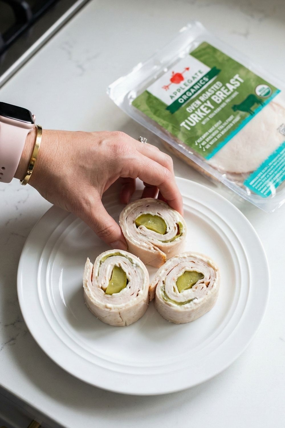 Three Applegate Organics turkey and pickle "sushi" roll-ups held in hand. A low-carb, high-protein finger food recipe for airplane meals.