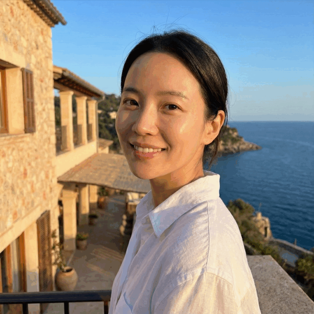 Portrait of a happy traveler with dewy, radiant skin smiling outdoors during golden hour on a balcony, showcasing the results of maintaining a consistent skincare routine while on vacation.