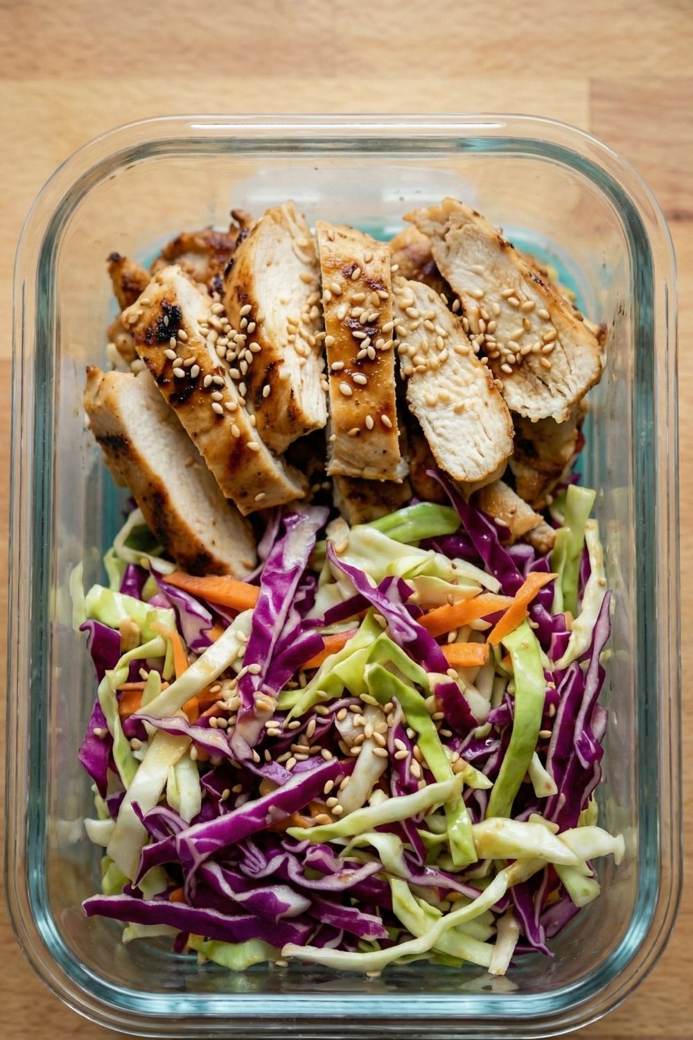 Overhead view of four open glass lunch containers filled with keto friendly sesame cabbage salad and sliced chicken.