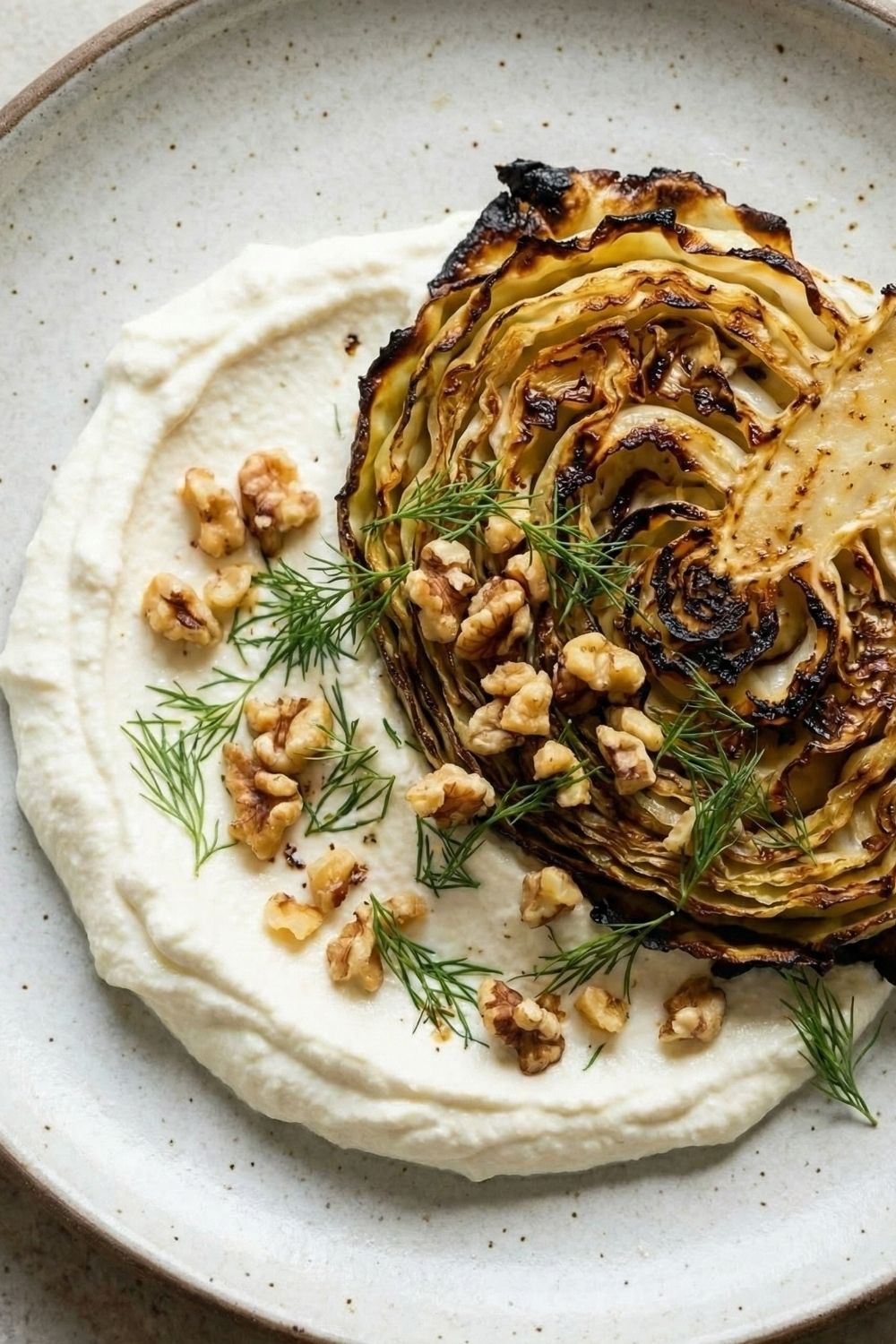 Close-up of a look into a tender roasted cabbage steak with creamy whipped feta and walnuts, showing the soft texture and crispy edges.