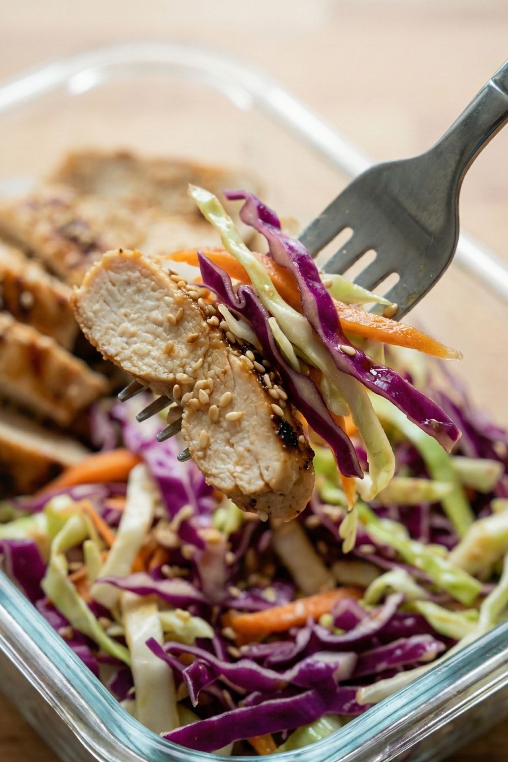 Fork lifting a piece of grilled chicken and crunchy cabbage salad showing the texture of the sesame dressing.