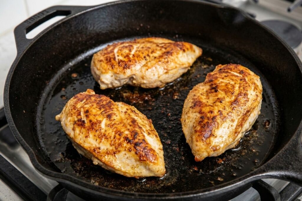 Golden brown seasoned chicken breasts searing in a Lodge cast iron skillet without overcrowding the pan.