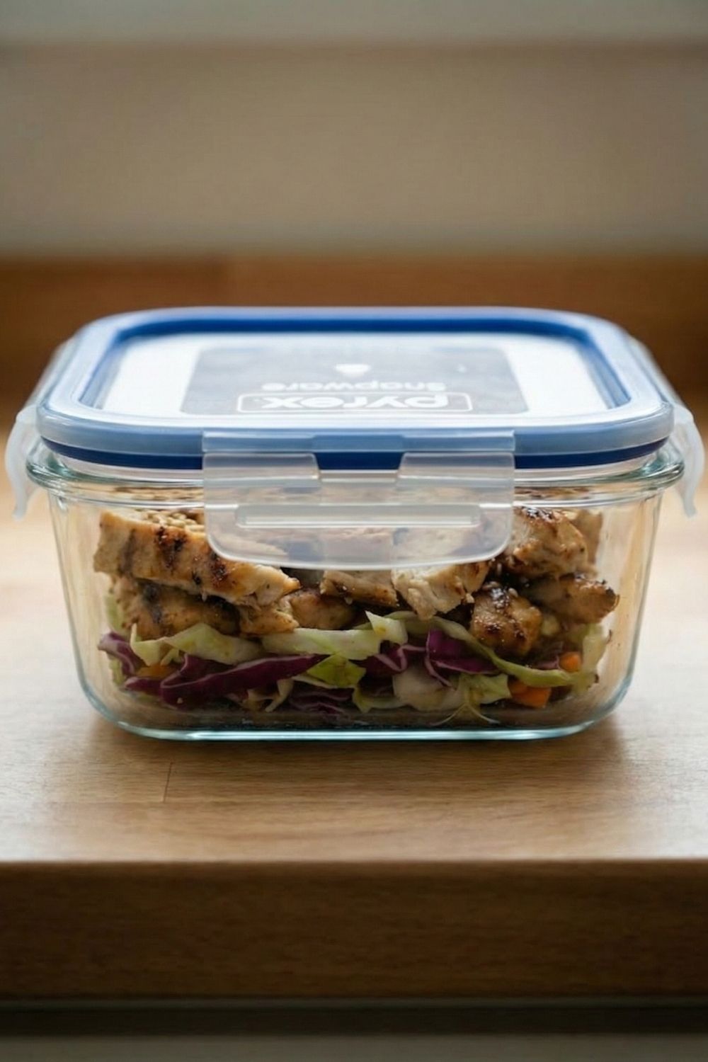 Side view of a sealed glass meal prep container with lid locked, showing layers of fresh cabbage salad ready for work lunch.