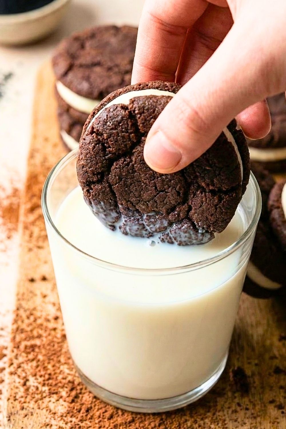 A professional stack of homemade zero sugar, gluten-free Oreo cookies on a white plate next to a glass of almond milk, featuring a dark and moody aesthetic.
