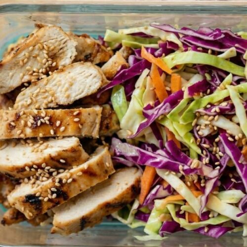 Close up top view of a single meal prep container featuring warm sesame cabbage salad topped with sesame seeds.