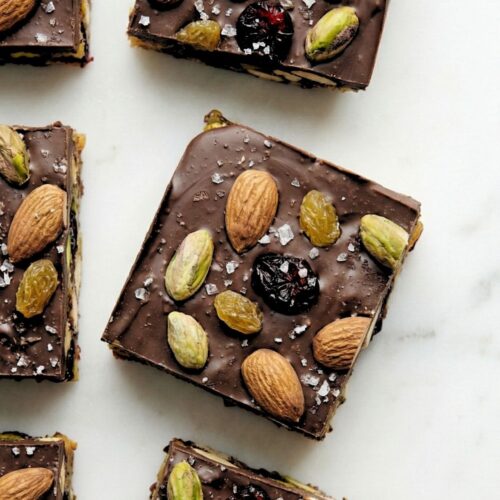 Top-down view of square-cut dark chocolate fruit and nut bars arranged in a grid on parchment paper.