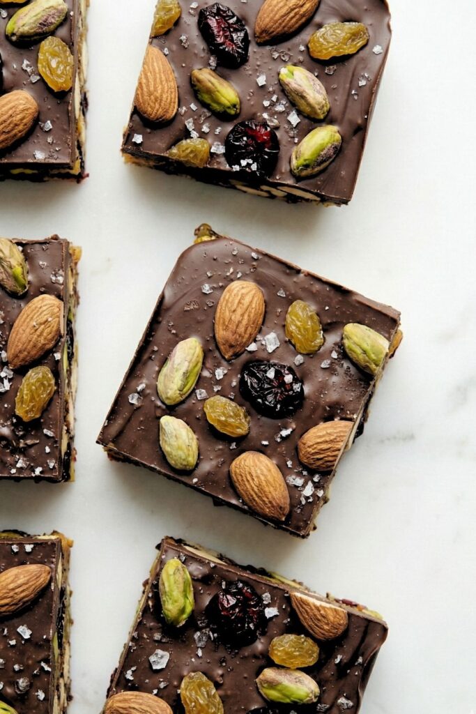 Top-down view of square-cut dark chocolate fruit and nut bars arranged in a grid on parchment paper.