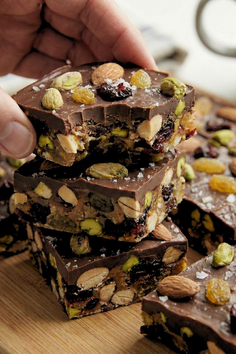 A vertical stack of three homemade dark chocolate fruit and nut bars showing the chunky texture of pistachios and raisins.