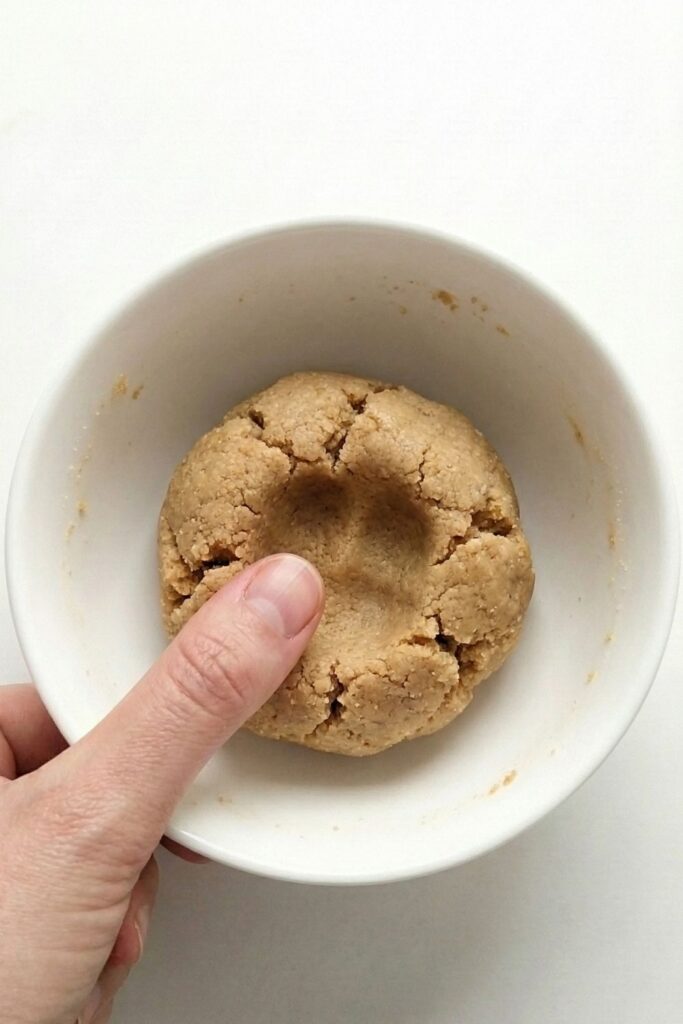 Hand pressing the crumbly mixture into a solid dough ball to hydrate the coconut flour.