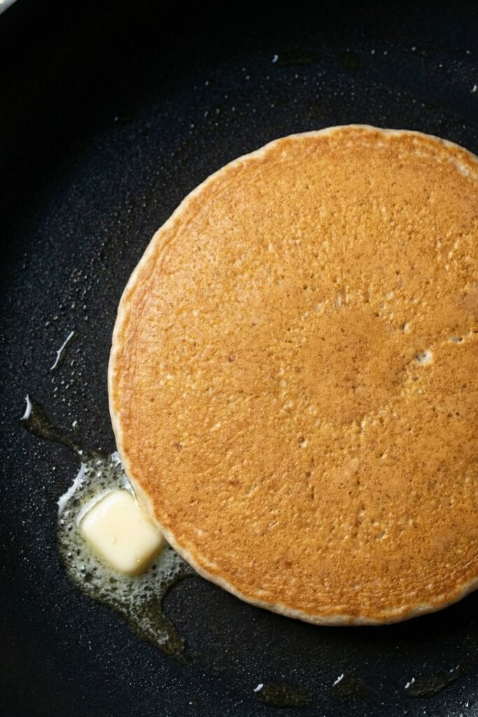 A perfectly flipped golden brown pancake cooking in the pan, showing the even color and soft texture.
