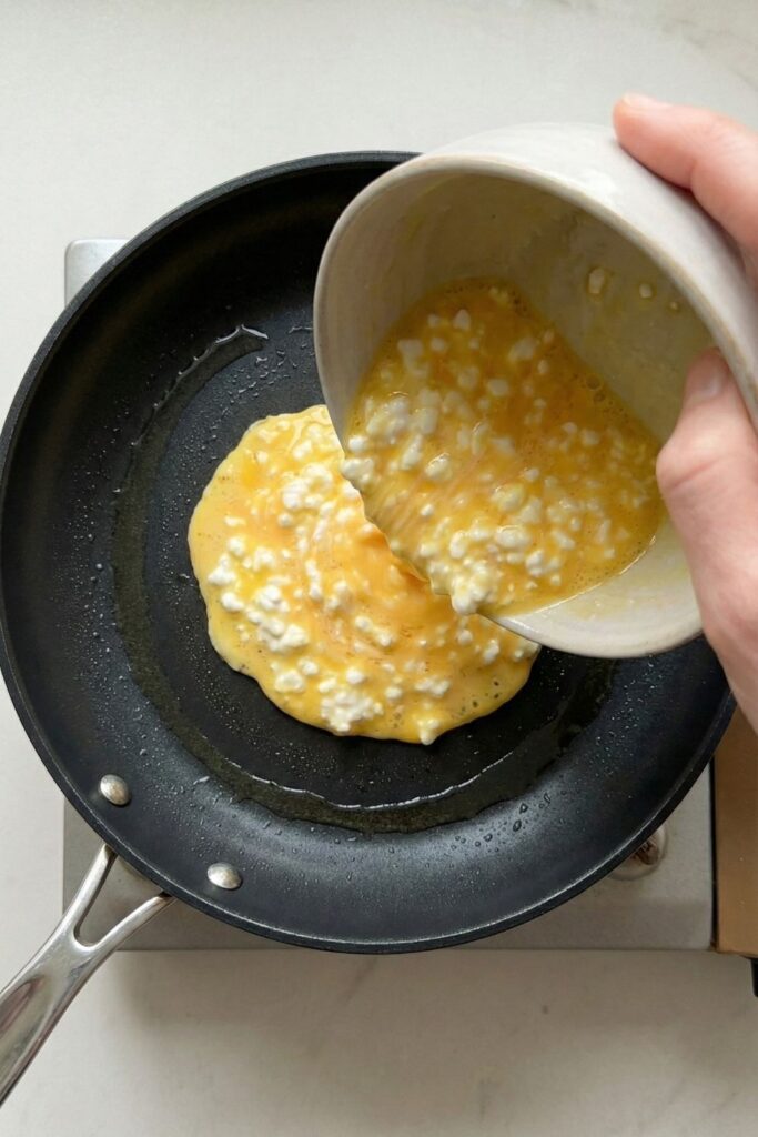 Pouring whisked cottage cheese and egg mixture into a hot non-stick skillet to start cooking soft scrambled eggs.