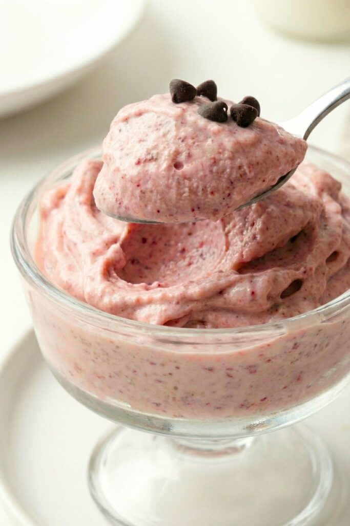 A close-up macro shot of a spoon taking a bite of ice cream, showing the velvety, dense texture inside with melted chocolate chips.