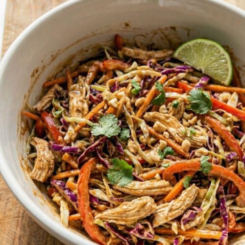 A delicious close-up of Thai Peanut Chicken Salad garnished with fresh cilantro, crushed peanuts, and a lime wedge, highlighting the creamy texture and vibrant crunch.