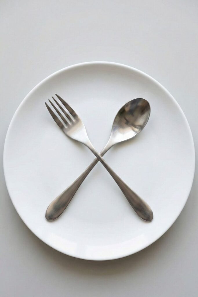 Alt Text: Weighted utensils crossed on a white plate to encourage mindful eating and weight loss.