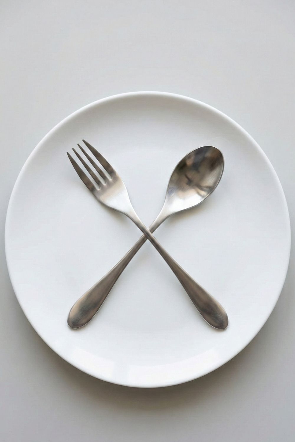 Alt Text: Weighted utensils crossed on a white plate to encourage mindful eating and weight loss.