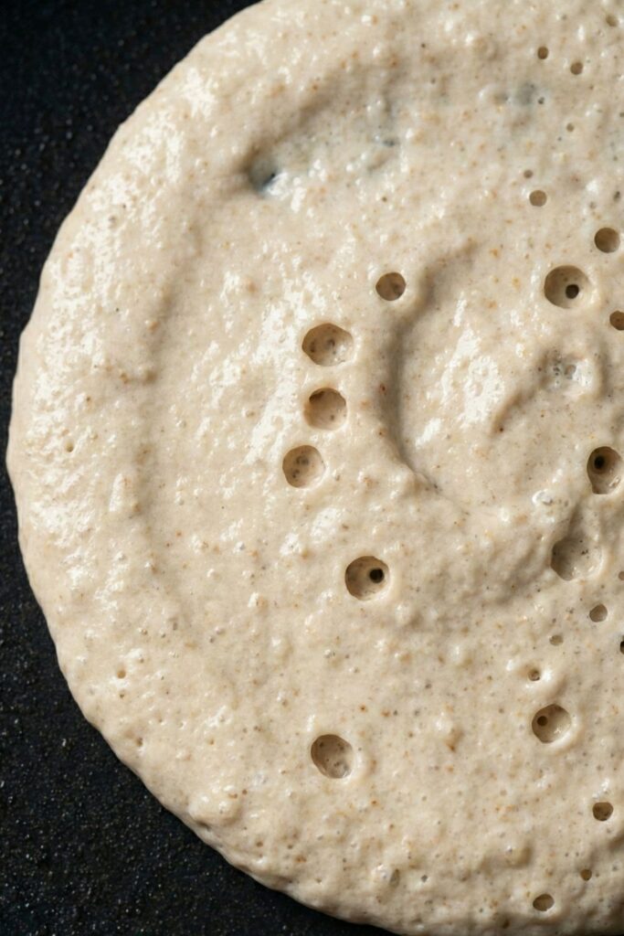 Close up of a pancake surface showing popped bubbles that stay open, the visual sign that gluten-free pancakes are ready to flip.