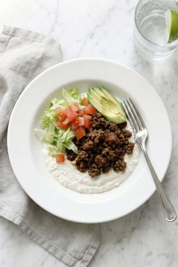 Lifestyle top-down shot of the taco dip served with a linen napkin, a fork, and a glass of sparkling water, ready for a healthy dinner or party snack.