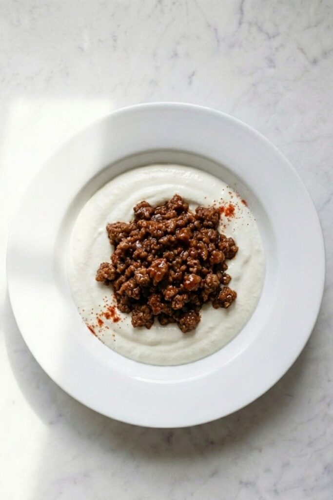 Hot seasoned ground beef spooned into the center of a whipped cottage cheese bowl, leaving a distinct white creamy rim visible around the edges.