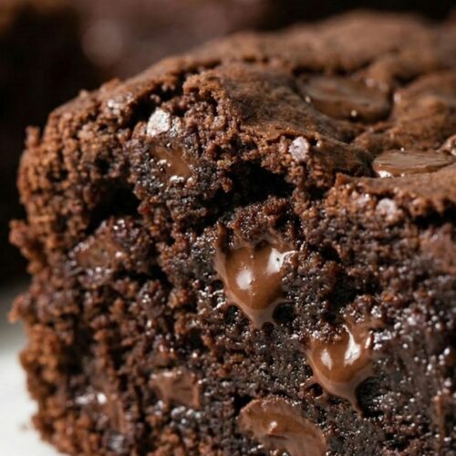 Extreme close-up of a sliced healthy brownie, highlighting the dense cocoa powder structure and shiny pockets of melted chocolate chips.