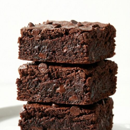 A stack of three high-protein sweet potato brownies on a white plate, showcasing moist crumbs and melted chocolate chips.