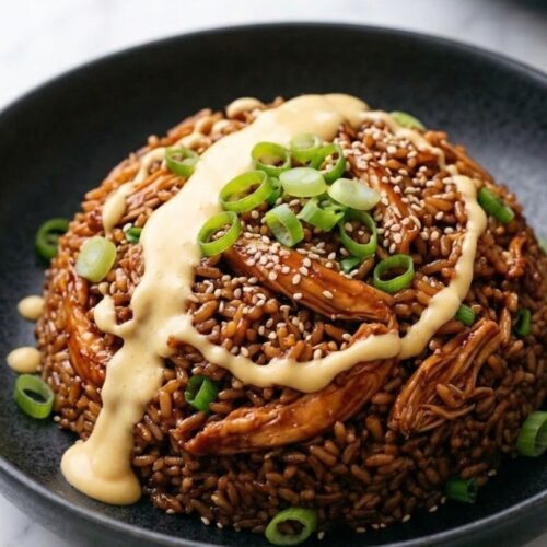 A dark matte bowl filled with high-fiber glossy teriyaki chicken and rice, topped with an elegant swoop of spicy yogurt sauce, bright scallions, and sesame seeds.
