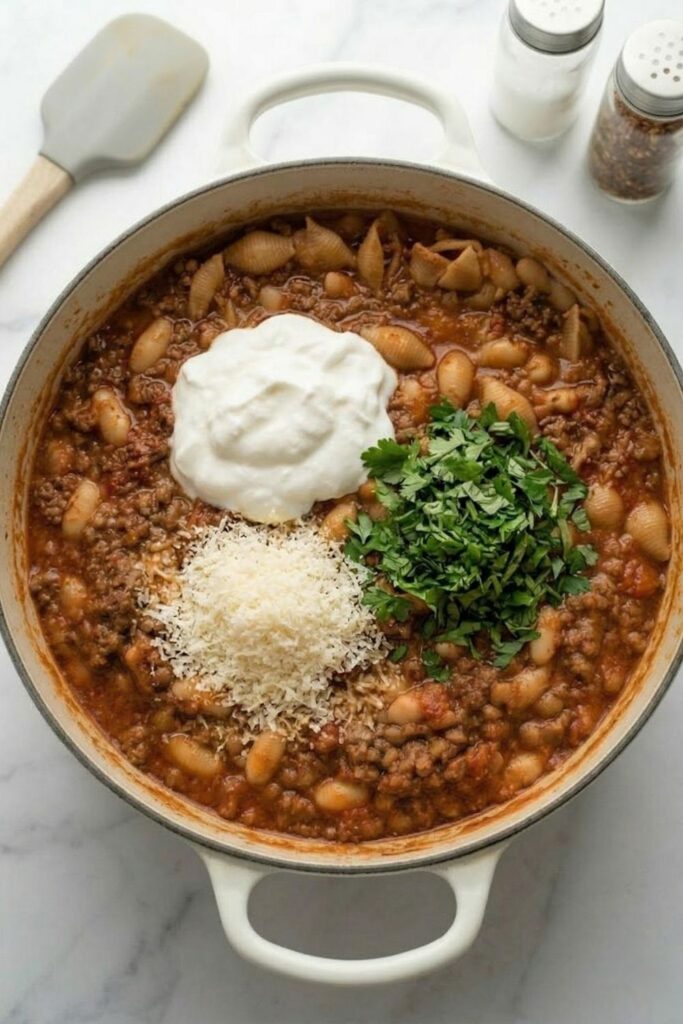 Whole milk skyr, grated parmesan cheese, and fresh herbs resting on top of a cooked one pot beef and lentil ragu before mixing.